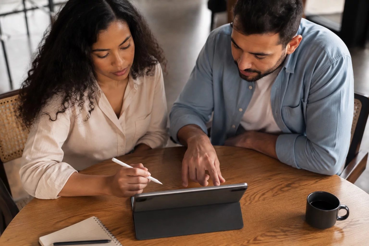 Duas pessoas revisando anotações em um tablet sobre uma mesa de madeira